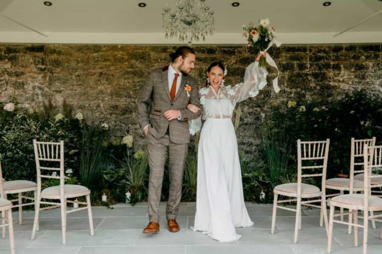 An interior lounge under a chandelier, the bride with her bouquet against stone, Briery Hill House