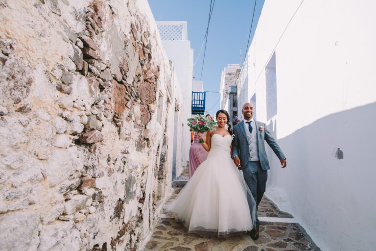 Bride and groom walking through the white lanes of a Milos village, Bright Blue Wedding And Events