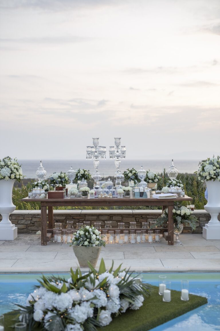 Long wedding table set beside a pool with white flowers, Bright Blue Wedding And Events