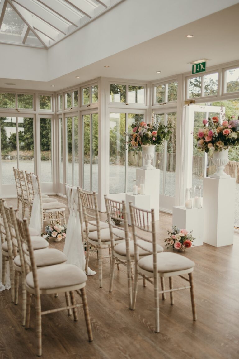 The Orangery set for a ceremony, limewash chiavari chairs and urns of blush and peach flowers, Broadoaks Country House