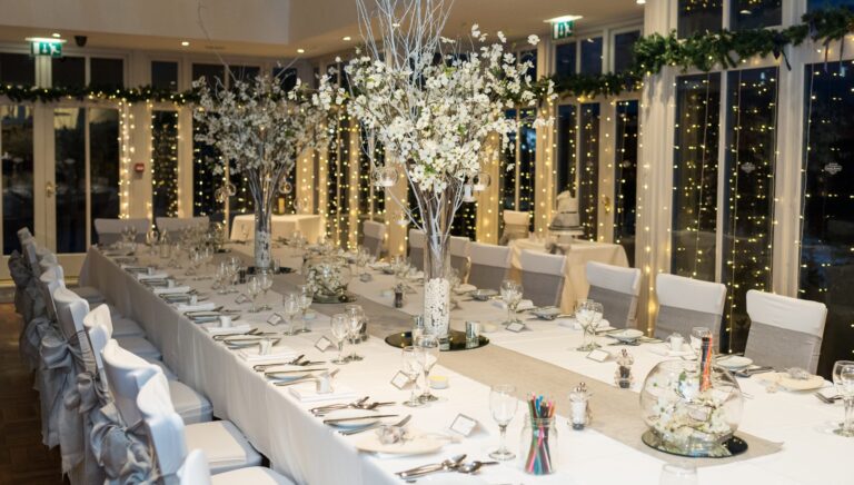 A long banqueting table under fairy lights with tall blossom trees down its length, Broadoaks Country House