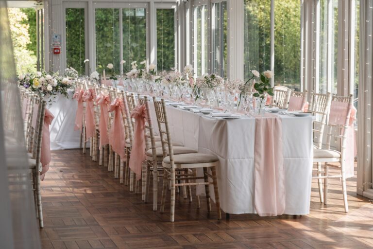 A long table dressed in blush with limewash chairs against the Orangery windows, Broadoaks Country House