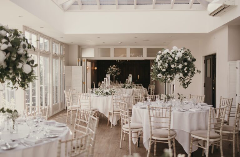 The Orangery laid with round tables, white linen and tall white and green florals, Broadoaks Country House
