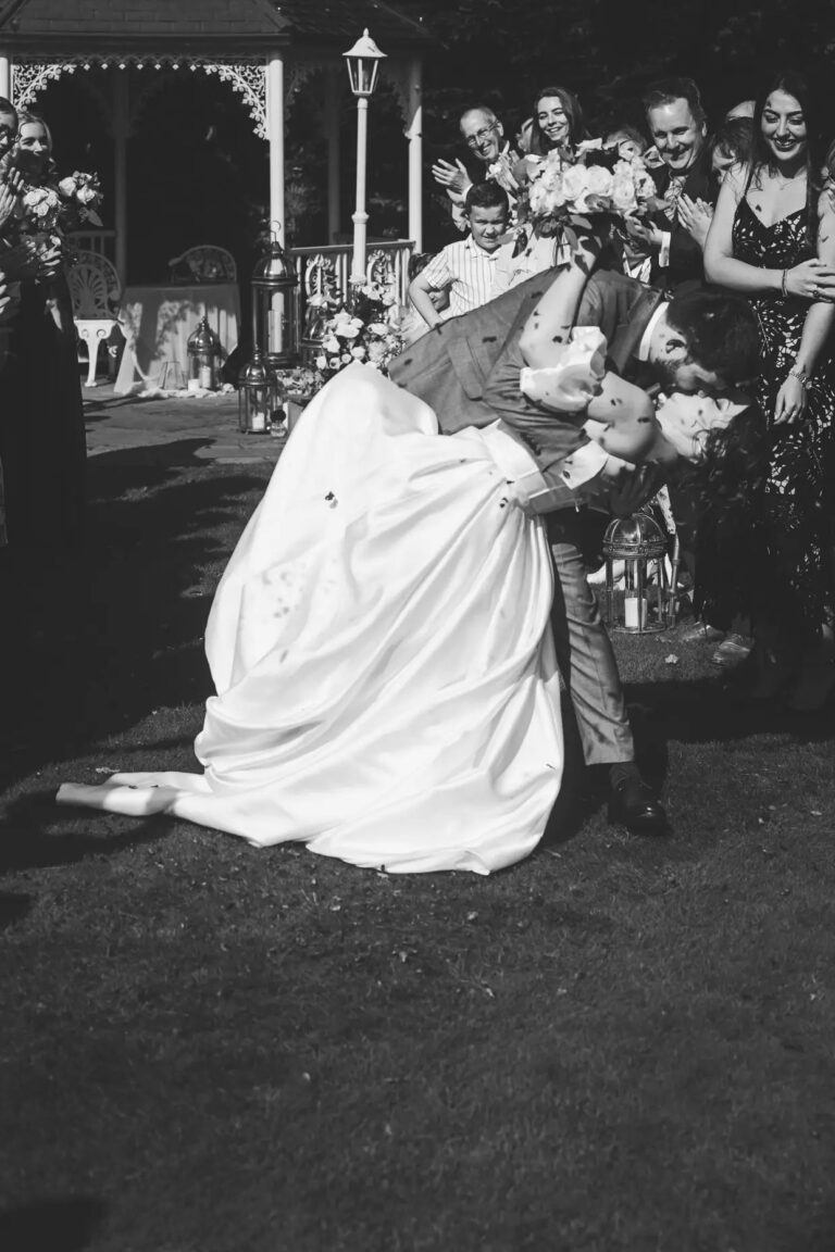 Black and white: the groom dips the bride for a kiss as guests throw confetti, the gazebo behind, Broadoaks Country House