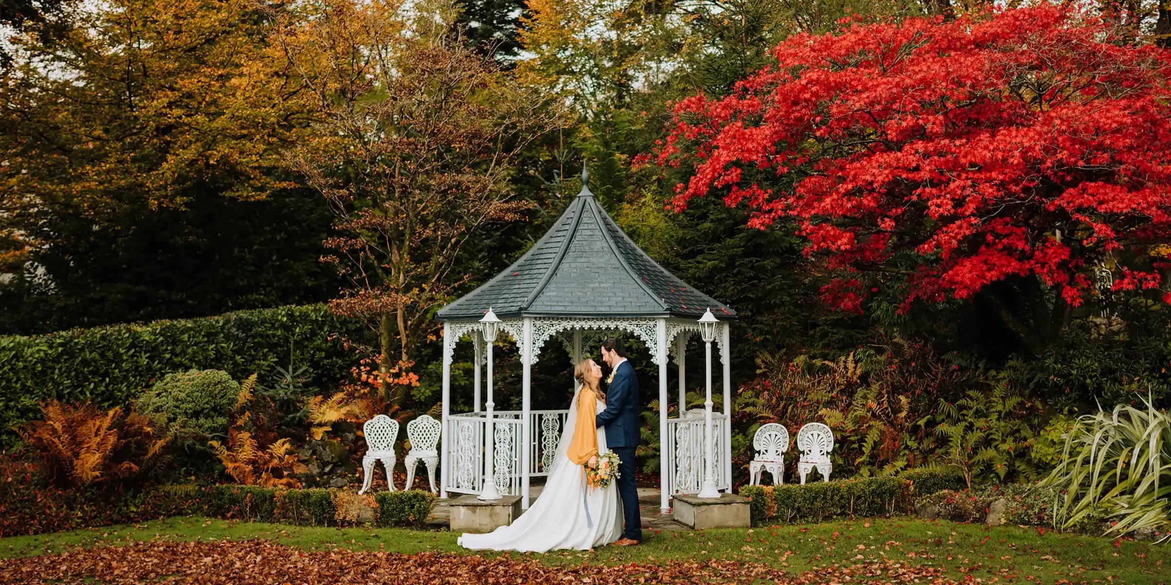 The couple facing each other in the white Victorian gazebo, scarlet acer and autumn borders behind, Broadoaks Country House