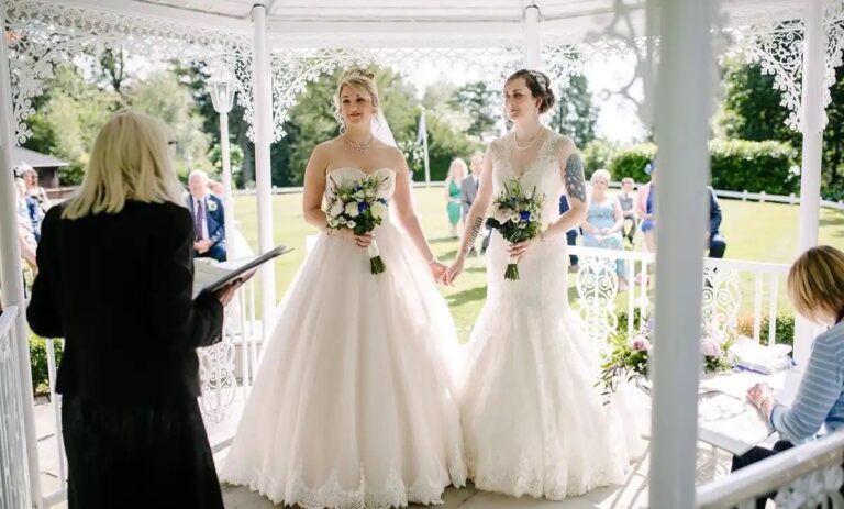 Two brides holding hands before the registrar in the Orangery, Broadoaks Country House