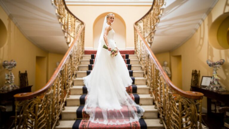 A bride with a long veil standing on the Hall's double staircase, between gilded balustrades, Brocket Hall