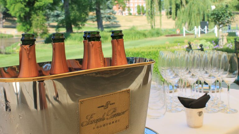 Bottles of rose Champagne in a silver ice bucket on a table outdoors, with the lake and willows behind, Brocket Hall