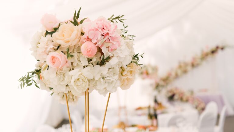 A tall arrangement of pale pink roses and hydrangea on a gold stand inside a white marquee, Brocket Hall