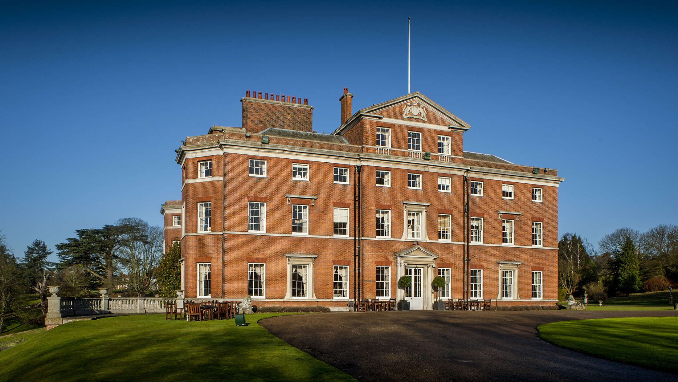 The red-brick front of Brocket Hall under a clear sky, with the lawn and the curve of the drive before it, Brocket Hall