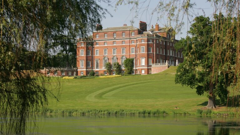 Brocket Hall on its rise above the Broadwater, seen across the water between willow and mature trees, Brocket Hall