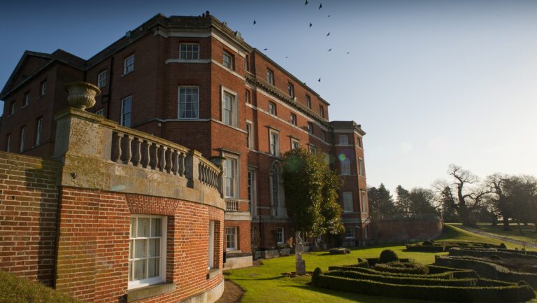 The side of the Hall from its balustraded terrace, looking down to a clipped box parterre in low sun, Brocket Hall