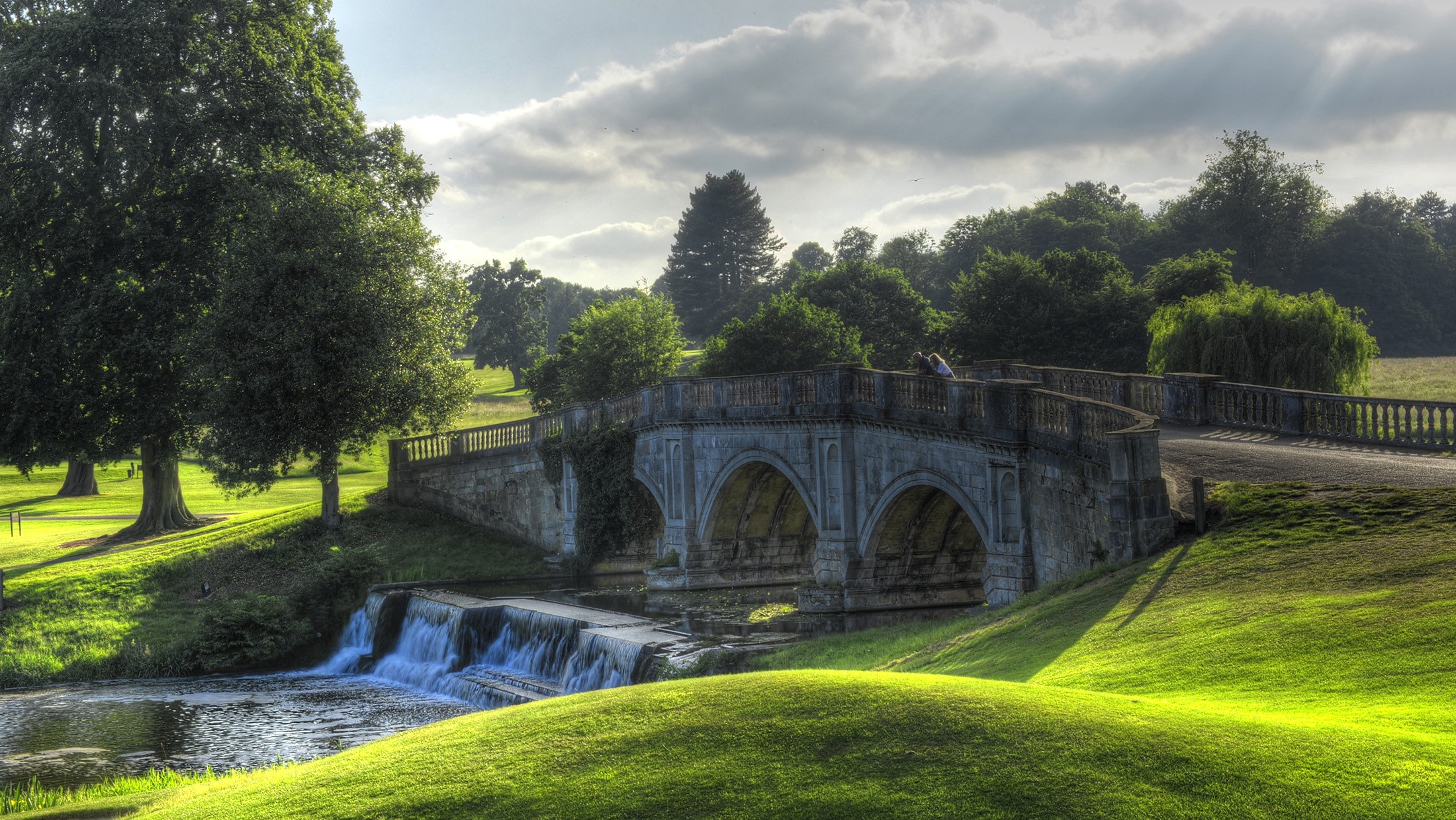 The three-arched stone Paine Bridge over the river, with a weir below it and parkland rising behind, Brocket Hall