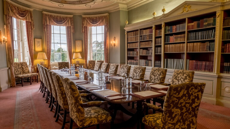 The Library at the bayed west end of the Hall, with its tall bookcases and a long table under the windows, Brocket Hall