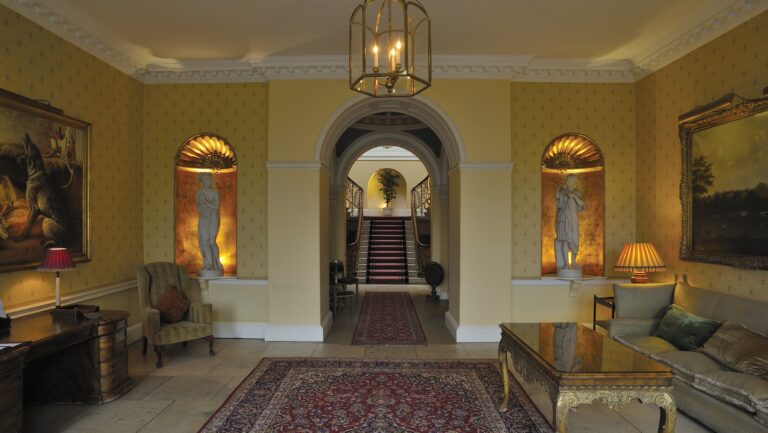 The entrance hall, with statues in lit shell niches either side of an arch leading through to the main staircase, Brocket Hall