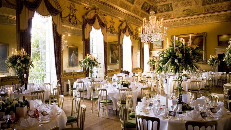 The Ballroom laid for a wedding breakfast with round tables, tall flower arrangements and chandeliers under the painted ceiling, Brocket Hall