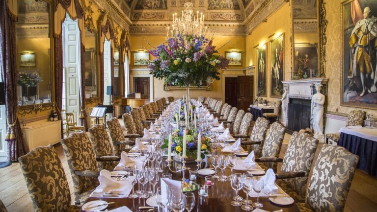 The Prime Minister's Table, a single long table laid down the Ballroom with upholstered chairs and a floral centrepiece, Brocket Hall