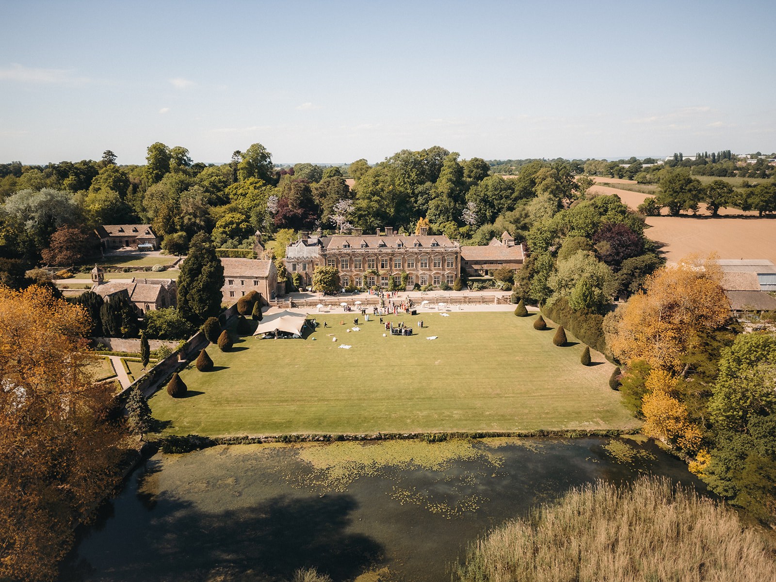 Aerial view over the lake and the long south lawn to the house, with the stables, church and Somerset farmland beyond, Brympton House