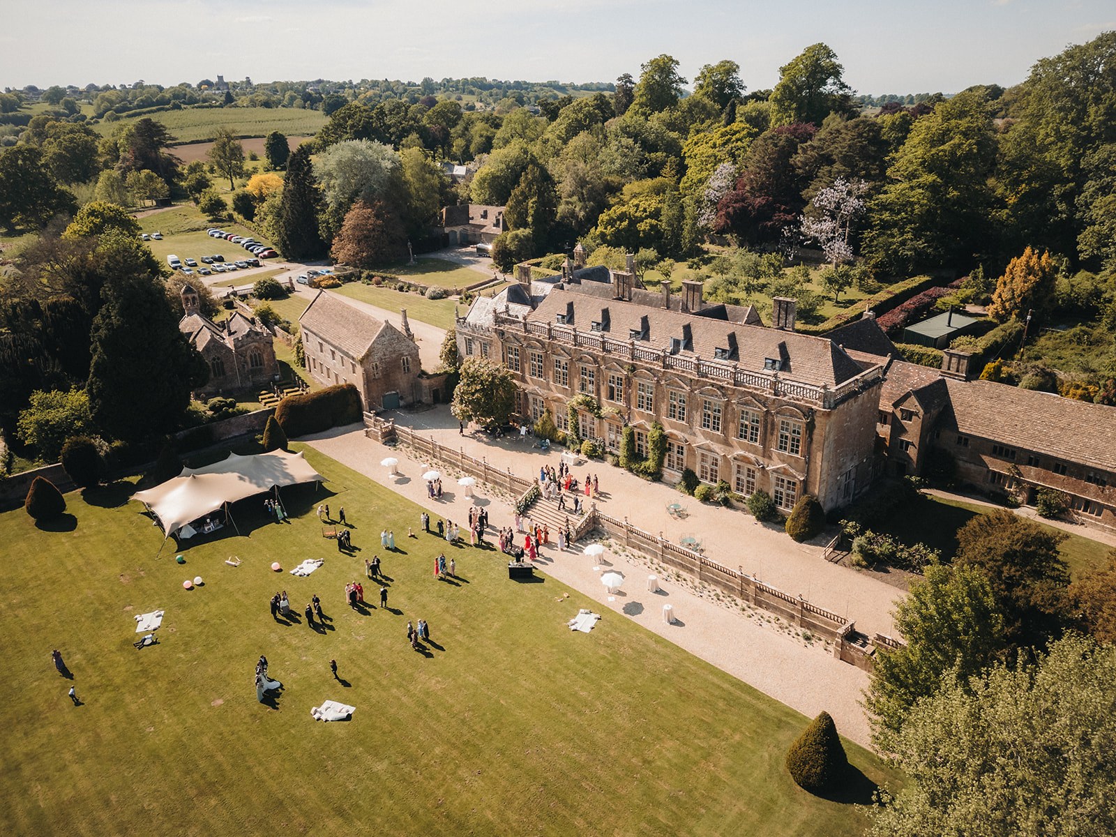 The house, forecourt and south lawn from the air during a summer wedding, with a stretch tent on the lawn, Brympton House