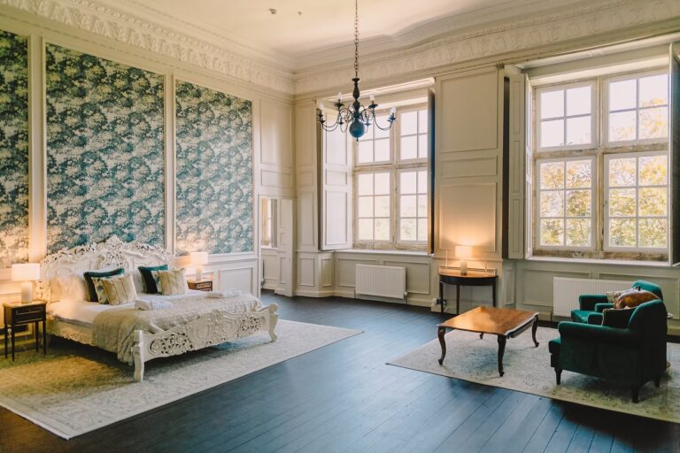 The Honeymoon Suite, a high-ceilinged room with leaf-pattern wall panels, a carved white bed and two tall windows, Brympton House