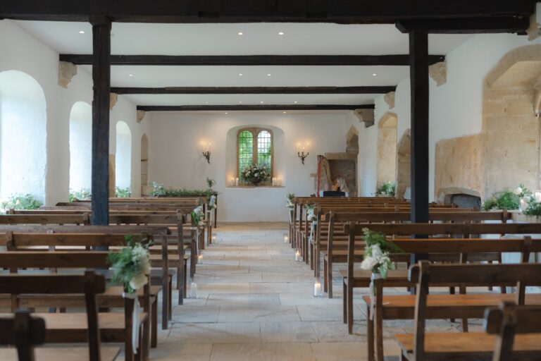 The Chapel set for a civil ceremony, with timber posts and beams, wooden pews and a flagstone aisle, Brympton House