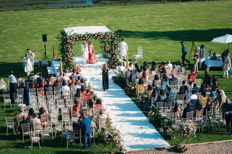 An outdoor ceremony on the lawn seen from above, with a flower-covered mandap and a long white aisle, Brympton House