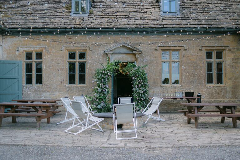 The Stables courtyard with deckchairs, picnic benches and a doorway garlanded with greenery, Brympton House