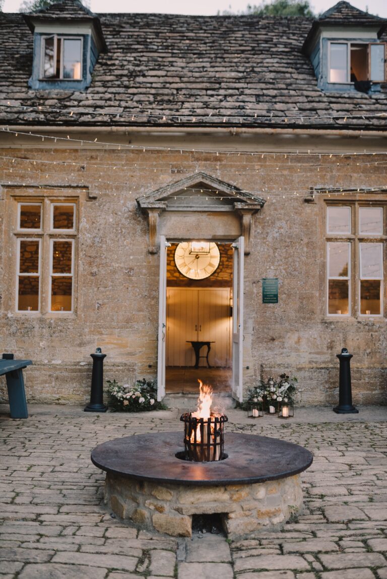 The Stables doorway with its pediment and clock, and a lit fire pit on the flagstones in front, Brympton House