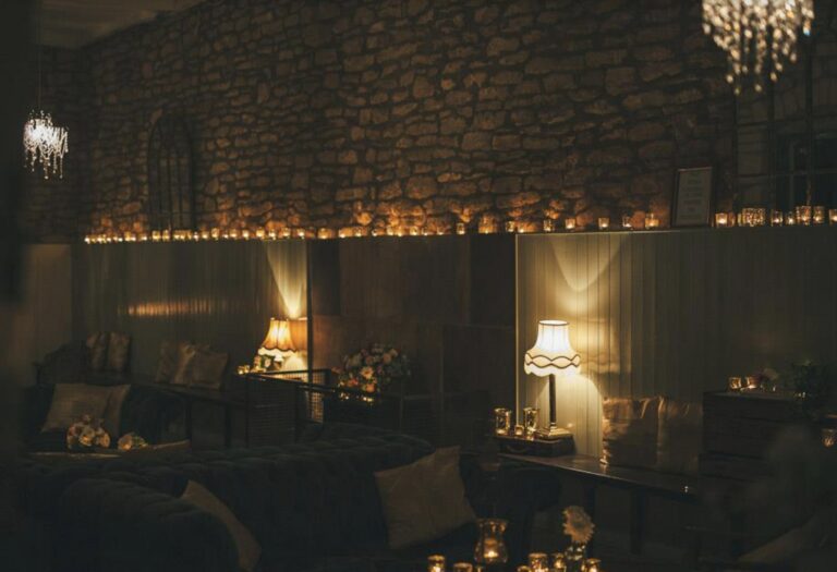 A dim lounge with a rough stone wall lined with tea lights and lamps for the evening, Brympton House