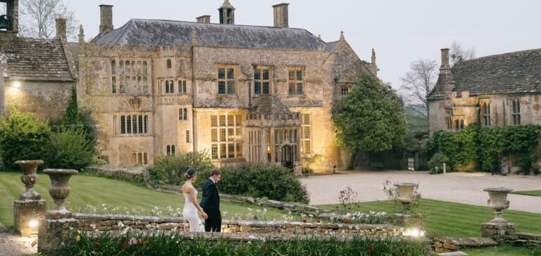 The house lit from within at dusk, seen from the garden with stone urns along the terrace, Brympton House