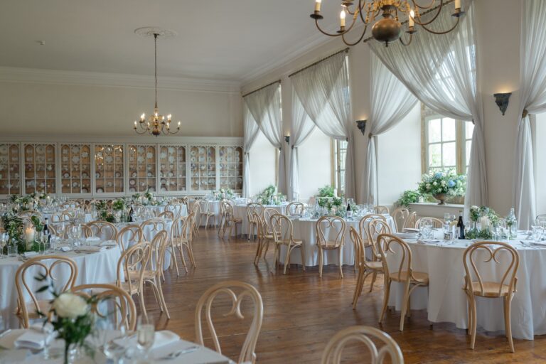 The Ballroom laid with round tables and bentwood chairs, white curtains at the south-facing windows, Brympton House