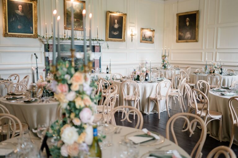 The Salon laid with round tables, candelabra and flowers beneath panelled walls hung with portraits, Brympton House