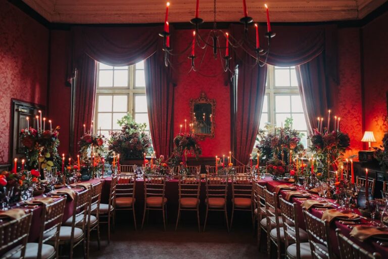 The red-walled State Dining Room set for a candlelit dinner, with red candles in the chandeliers, Brympton House