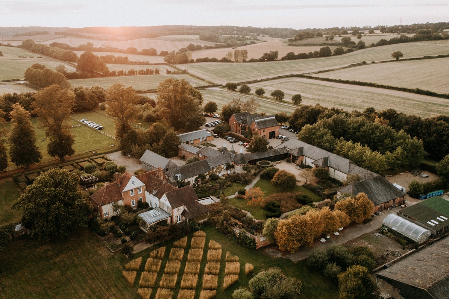 Aerial view of the Bury Court buildings and walled gardens at sunset, with open Hampshire farmland beyond, Bury Court