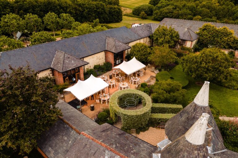 The courtyard from above, set with tables under two white stretch tents between the barn ranges and a round clipped hedge, Bury Court