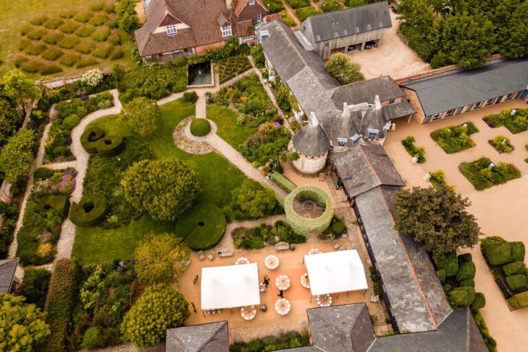 Overhead view of the courtyard garden, the barn roofs and the oast house cones, with guests gathering by the tents, Bury Court
