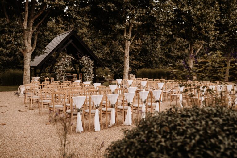 Chairs dressed with white sashes facing the oak-framed arbour in the garden ceremony space, Bury Court