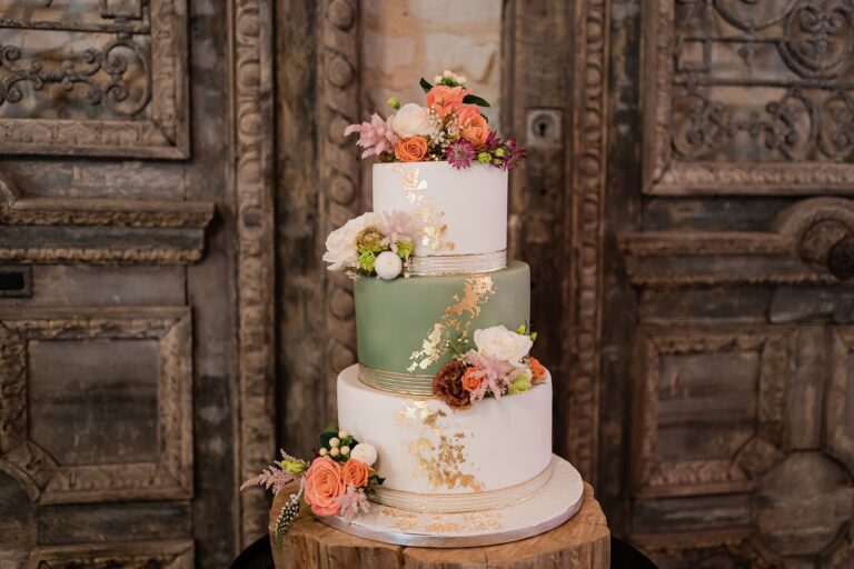 A three-tier cake with peach and orange flowers in front of a carved wooden door, Bury Court