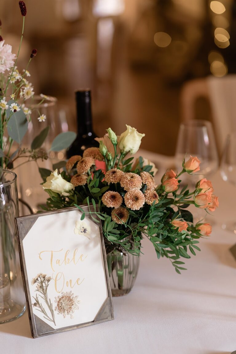 Table flowers in soft peach tones beside a table-number card, Bury Court