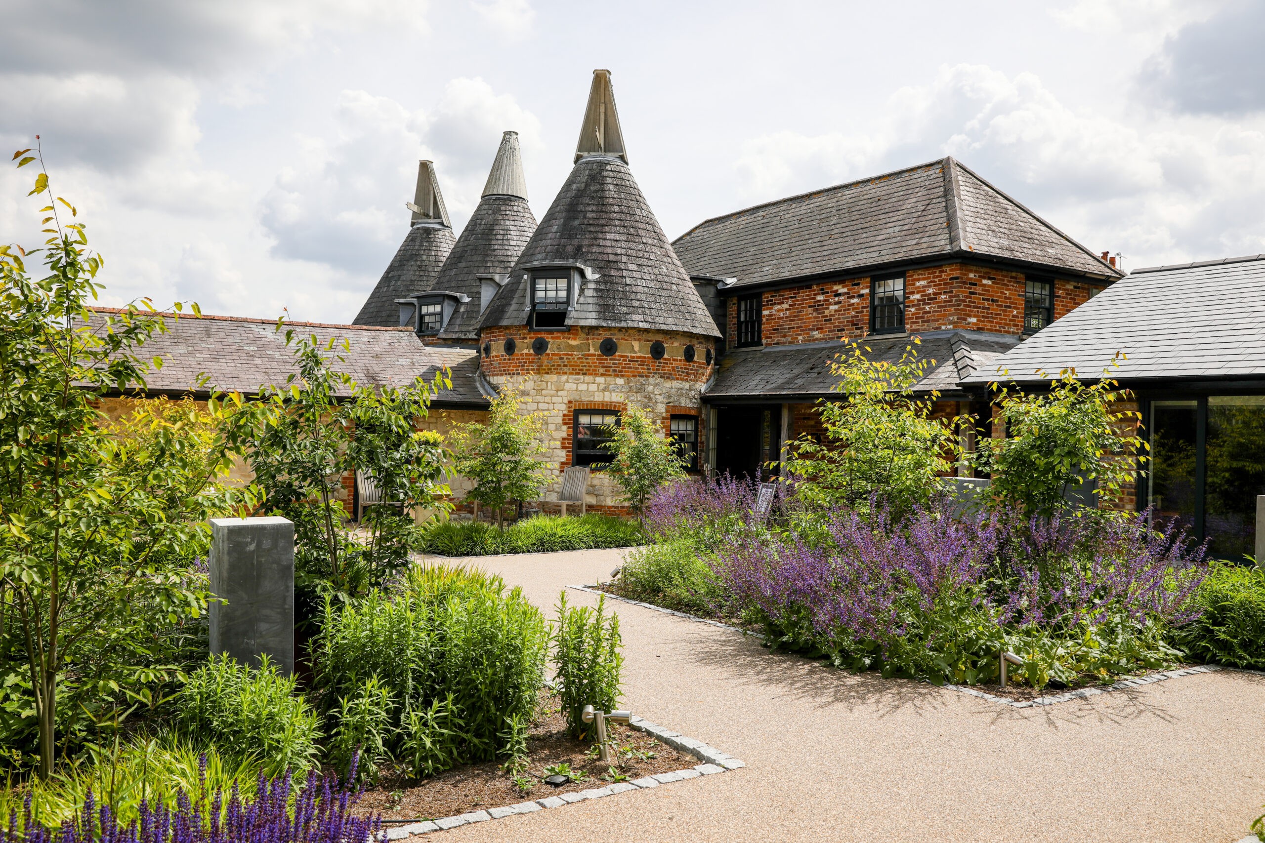 The three oast house roundels and the brick Oast House beside the planted courtyard, with lavender and gravel paths, Bury Court