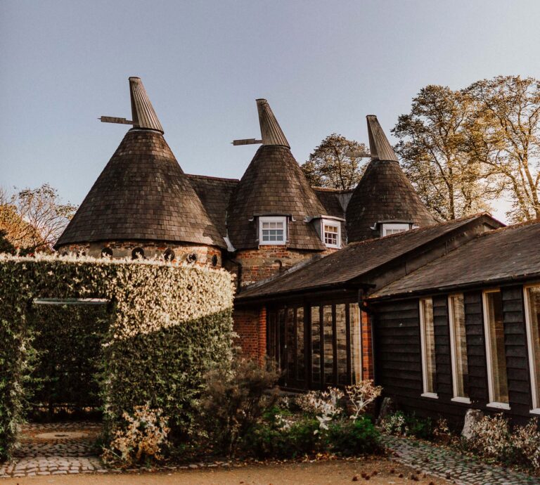Oast house cones above the black weatherboarded range and clipped hedges in autumn light, Bury Court