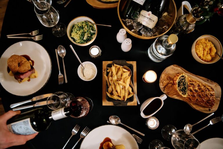 Roast dishes, sides, fries and wine on a dark tablecloth, seen from above, Bury Court