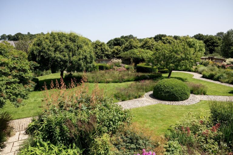 The gardens in summer, with clipped domes, a curving lawn and mixed perennial planting, Bury Court