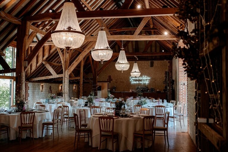 The Barn set for a wedding breakfast, with round tables, crystal chandeliers and the oak roof trusses, Bury Court