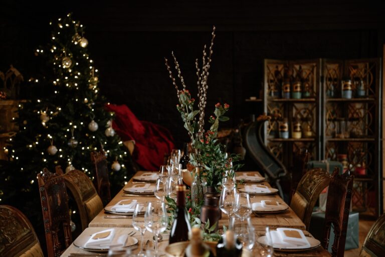 A long dinner table laid with glassware and winter greenery beside a lit Christmas tree, Bury Court