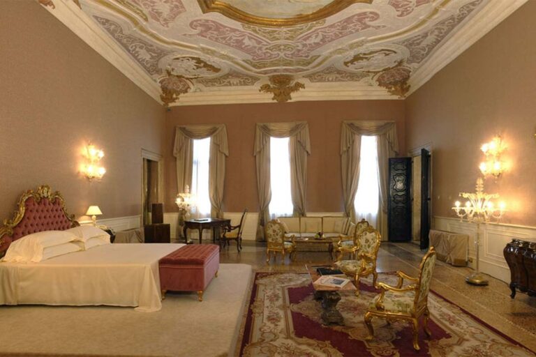 A suite beneath Sebastiano Ricci's frescoed ceiling, dressed in red and gold, Ca' Sagredo Hotel