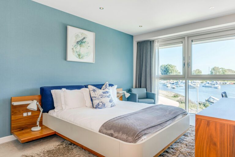 A suite bedroom in blue and white with a corner window looking over the moorings, Captain's Club Hotel & Spa