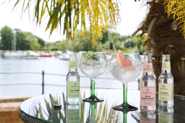 Gin and tonics with tonic bottles on a terrace table, looking across the river to moored yachts, Captain's Club Hotel & Spa