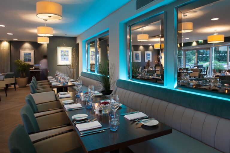 A long table laid in the Club Restaurant, with banquette seating, pendant lamps and windows on to the river, Captain's Club Hotel & Spa