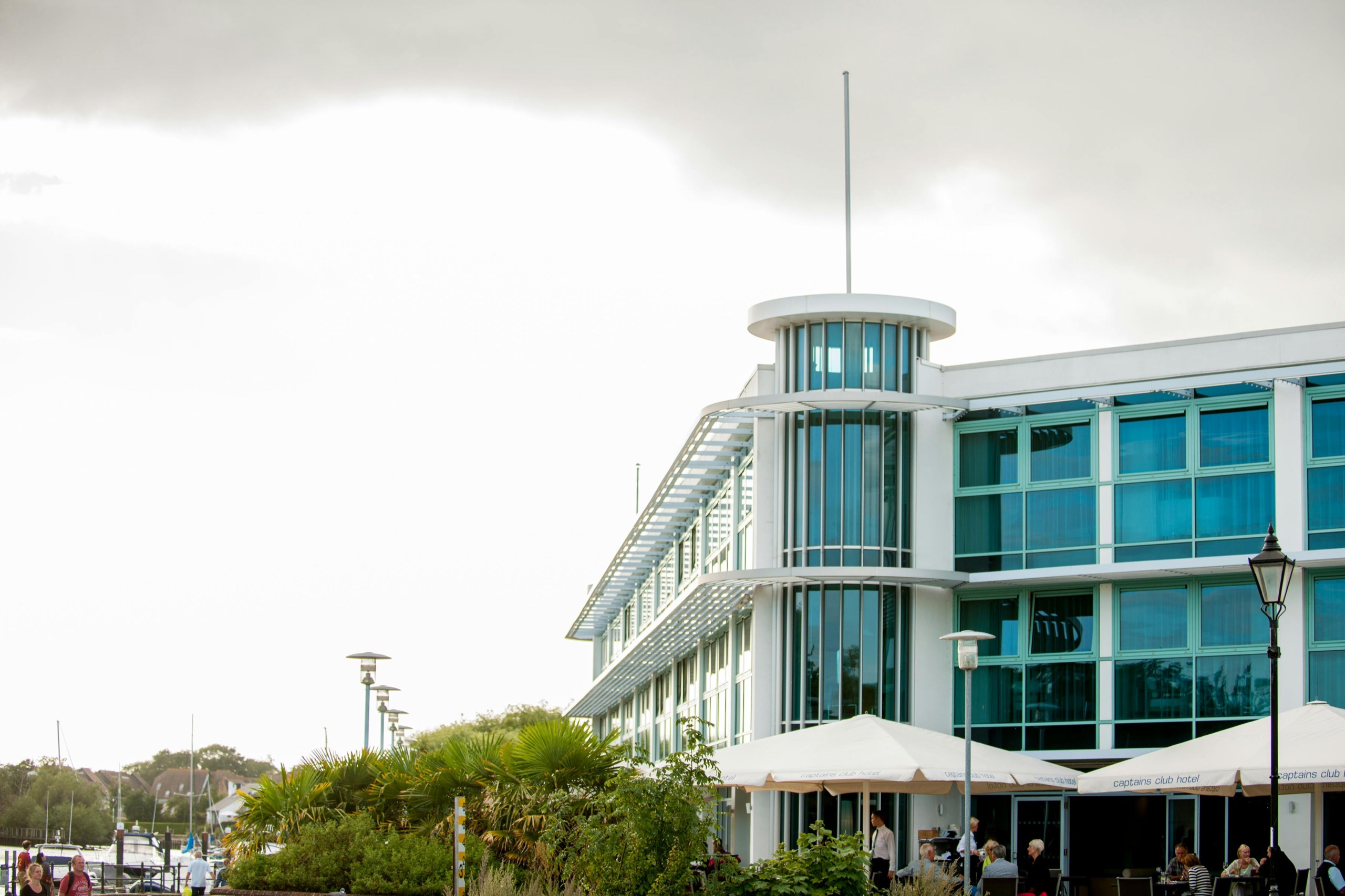 The hotel's round glazed stair tower and ship-like white and glass facade, seen from the quayside with the terrace parasols below, Captain's Club Hotel & Spa